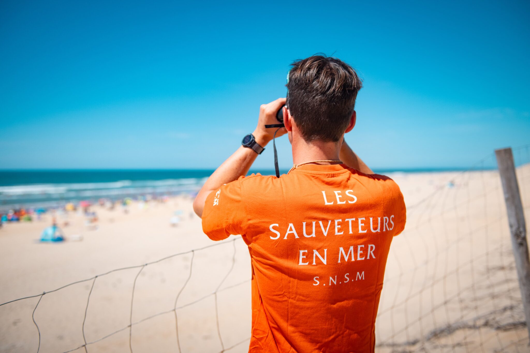 Homme posant de dos sur la plage avec des jumelles