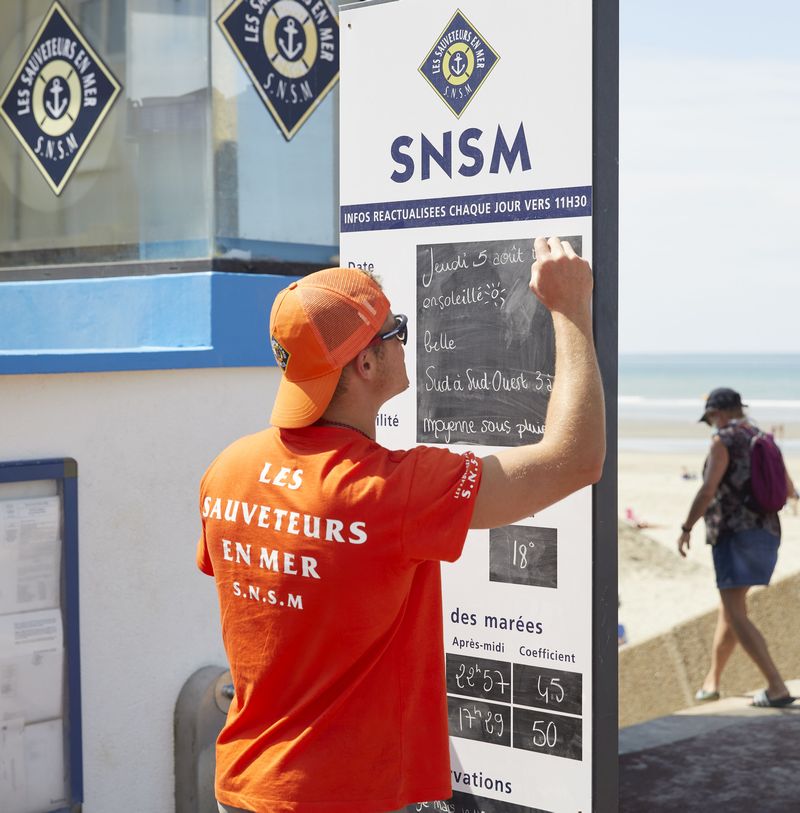 Nageur sauveteur en train d'écrire sur le panneau d'information devant un poste de secours